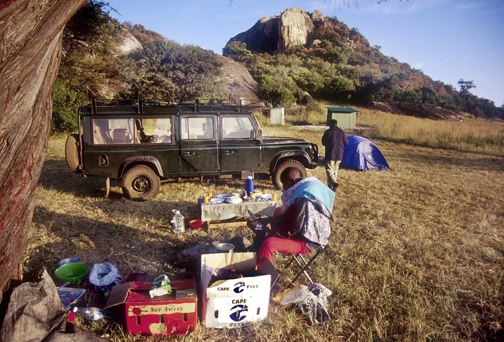 A documentary camp scene with a vehicle, supplies and people near the Lobo kopjes